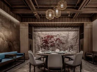 Modern restaurant dining room with a stone accent wall, wooden tables, and upholstered chairs.