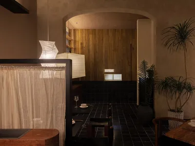 Industrial-style restaurant interior with exposed concrete ceiling, wood-paneled walls, and black-tiled floor.
