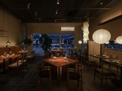 A modern restaurant interior featuring a wooden texture with tables, chairs, and decorative lighting.