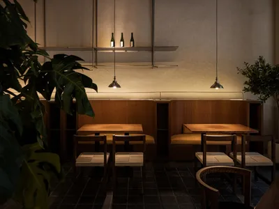 A minimalist restaurant interior with wooden tables, fabric chairs, and concrete accents.