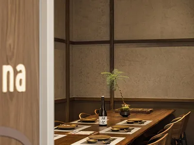 Modern restaurant interior with wooden tables, chairs, and a bottle of sake.