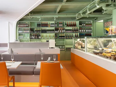 Modern restaurant interior with orange floor, white walls, concrete counter, and green shelving.