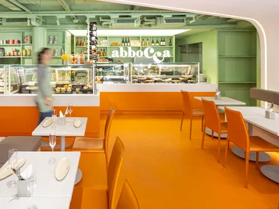 A modern restaurant interior with vibrant orange and green colors, featuring tables, chairs, and a counter with food displays