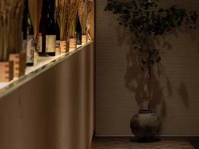現代簡約餐廳室內，搭配木質元素、擺放酒瓶的層架，以及綠色植物。