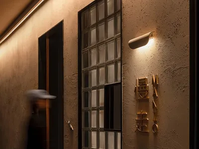 A modern restaurant entryway featuring glass block walls and a brass nameplate mounted on a textured beige wall.