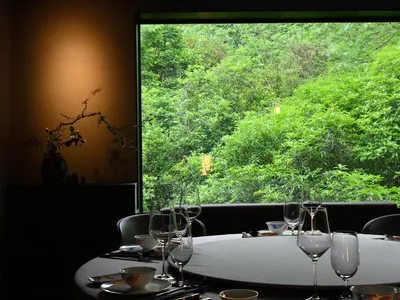 Modern restaurant setting featuring glassware and greenery outside a large window.