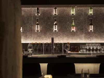 A modern restaurant bar with a sleek, contemporary concrete counter and wall-mounted drinks display.