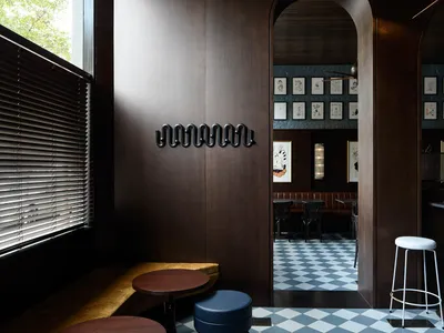 Modern restaurant interior with wooden seating, marble tables, and checkered-tiled floor.