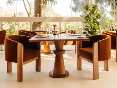 A modern restaurant interior with wooden furniture, featuring large windows and a view of the outdoors.