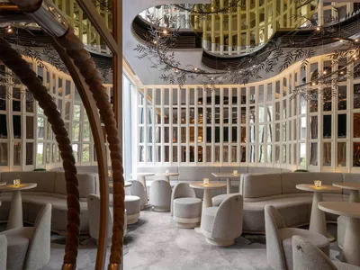 A modern restaurant bar with sleek, curved seating, round tables, and glass walls.