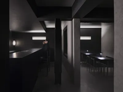 A minimalist restaurant interior with black concrete walls and lighting fixtures