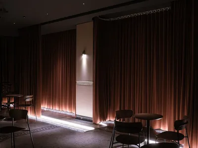 A modern restaurant interior with red curtains, wooden tables, and chairs.