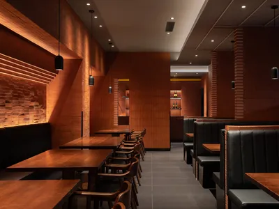 Modern industrial restaurant interior featuring wood tables, black leather seating, and brick walls.
