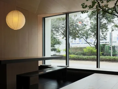 Minimalist modern restaurant interior with large windows, wooden seating and tables, and a lantern light hanging overhead.