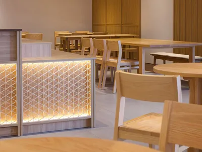 A modern restaurant interior featuring wooden tables and chairs, illuminated by strategically placed lights within the ceilin