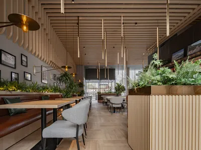 Modern restaurant interior with wooden paneling, green plants, and contemporary lighting fixtures.