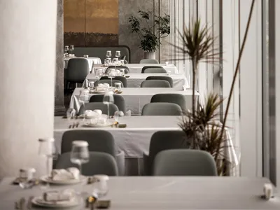 A minimalist restaurant interior with white walls, concrete columns, and large windows.