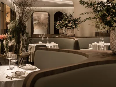 Modern restaurant dining room with white and gray decor, curved ceiling, and floral arrangements.