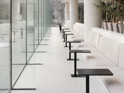 Modern restaurant interior featuring white marble tables and black chairs surrounded by large glass walls.
