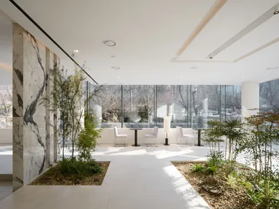 A modern, minimalist room featuring white marble walls, a table with white chairs, and a small garden with rocks and plants.