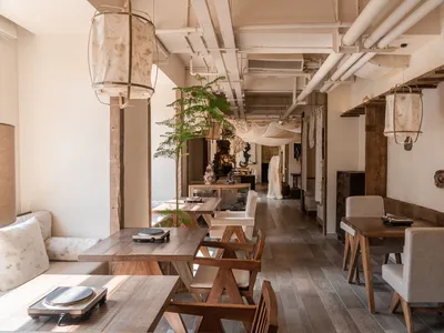Warm-toned photograph of a cafe interior with wooden furniture, concrete floors, and plants.