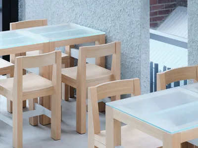 Industrial-style restaurant interior featuring wooden chairs and tables with glass tops.