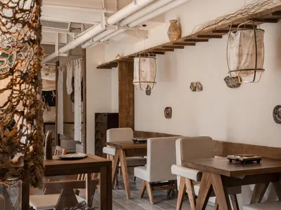 An industrial-style restaurant interior featuring wooden tables, fabric pendant lights, and clay decorations on the walls.