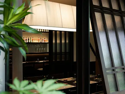A modern restaurant interior with dark wood elements, glass windows, and fabric lighting.