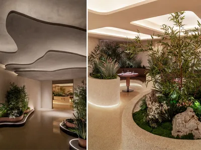 A modern restaurant interior featuring concrete walls and floors, with plants and table arrangements.