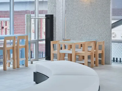 A minimalist restaurant interior featuring glass tables, wooden chairs, and a concrete textured wall.