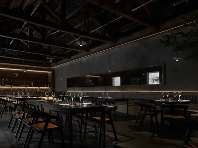 A dark, industrial-style restaurant with black steel chairs, concrete flooring, and wooden elements.