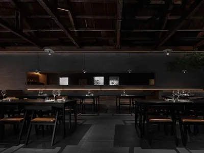A minimalist restaurant interior featuring concrete walls and dark tables and chairs.