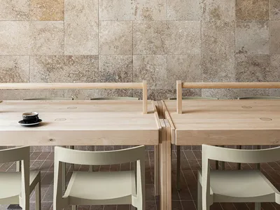 Modern restaurant interior with wooden tables, stone wall, and minimalist design.