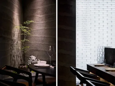 A serene restaurant interior featuring a textured concrete wall and minimalist dining setup.