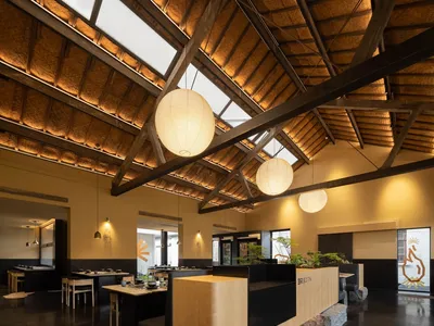A minimalist restaurant interior with a high ceiling, recessed lighting, and wooden materials.