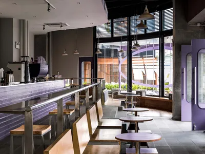 An image depicting the interior of a modern coffee shop with wooden seating, metallic hanging lights, and concrete walls.