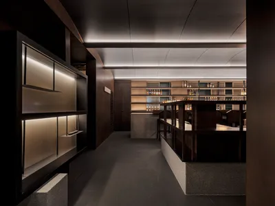 A modern restaurant bar with wooden interiors and shelves filled with bottles.