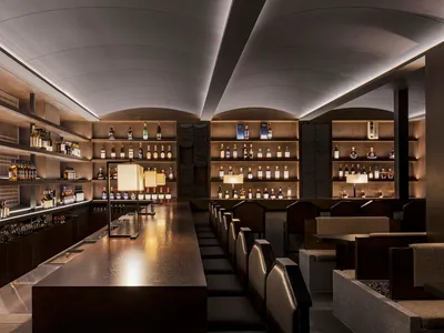 A modern restaurant bar with wooden counters and shelves filled with bottles.