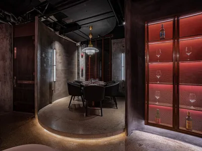 A modern restaurant interior featuring concrete flooring, glass walls, and metal accents.