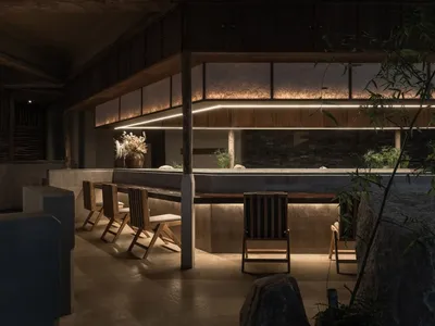 Modern minimalist restaurant interior featuring concrete, stone, and wood with warm lighting.