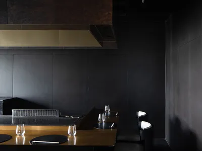 A minimalist design featuring black leather chairs, black metal table, and a black wall with a golden counter.