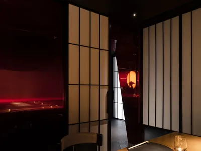 Modern restaurant interior with wooden curtains, red light, and sleek furniture.