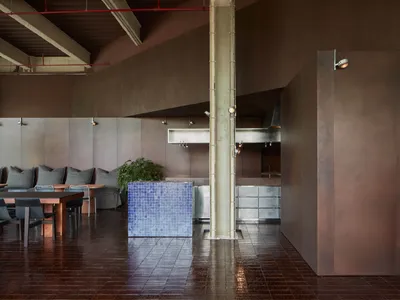 Industrial restaurant interior with metallic textured walls, matte tiled flooring, hardwood beams, and seating areas.