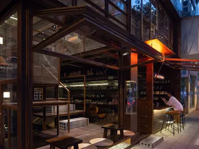 An industrial-style restaurant interior featuring wooden tables, glass shelves, and concrete surfaces.
