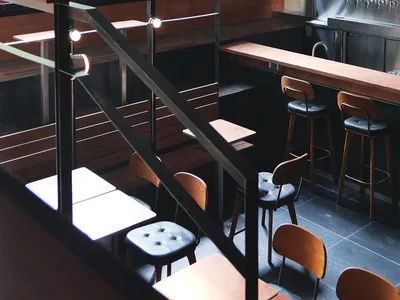 Industrial-themed restaurant bar area with wooden tables, metal railings, and glass windows