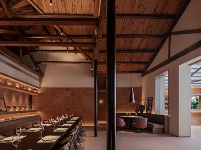 Modern industrial restaurant interior with wooden flooring and ceiling beams, featuring long communal dining table and seatin