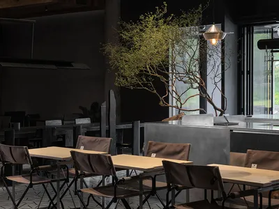 Industrial-style restaurant interior with metal accents, concrete walls, and wooden tables and chairs.