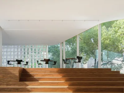 Modern restaurant interior with glass windows, wooden stairs, and tables set up for guests.