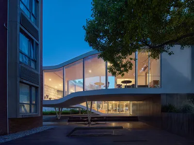 A modern restaurant exterior featuring a glass facade and a concrete structure, set against the night sky.