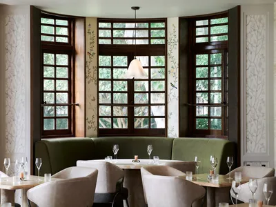 An elegant restaurant interior with green sofas, glass tables, and wooden accents